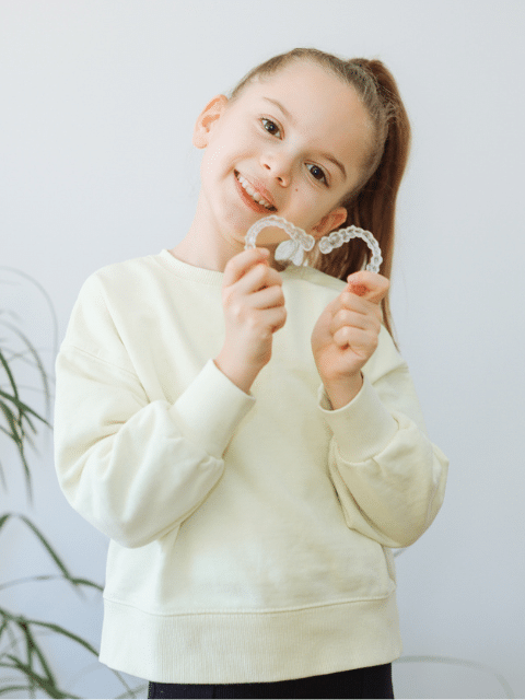 A young girl holding a clear aligner | Harwell & Cook Orthodontics