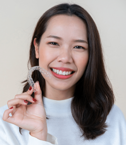 A smiling woman holding a clear dental aligner. | Harwell & Cook Orthodontics
