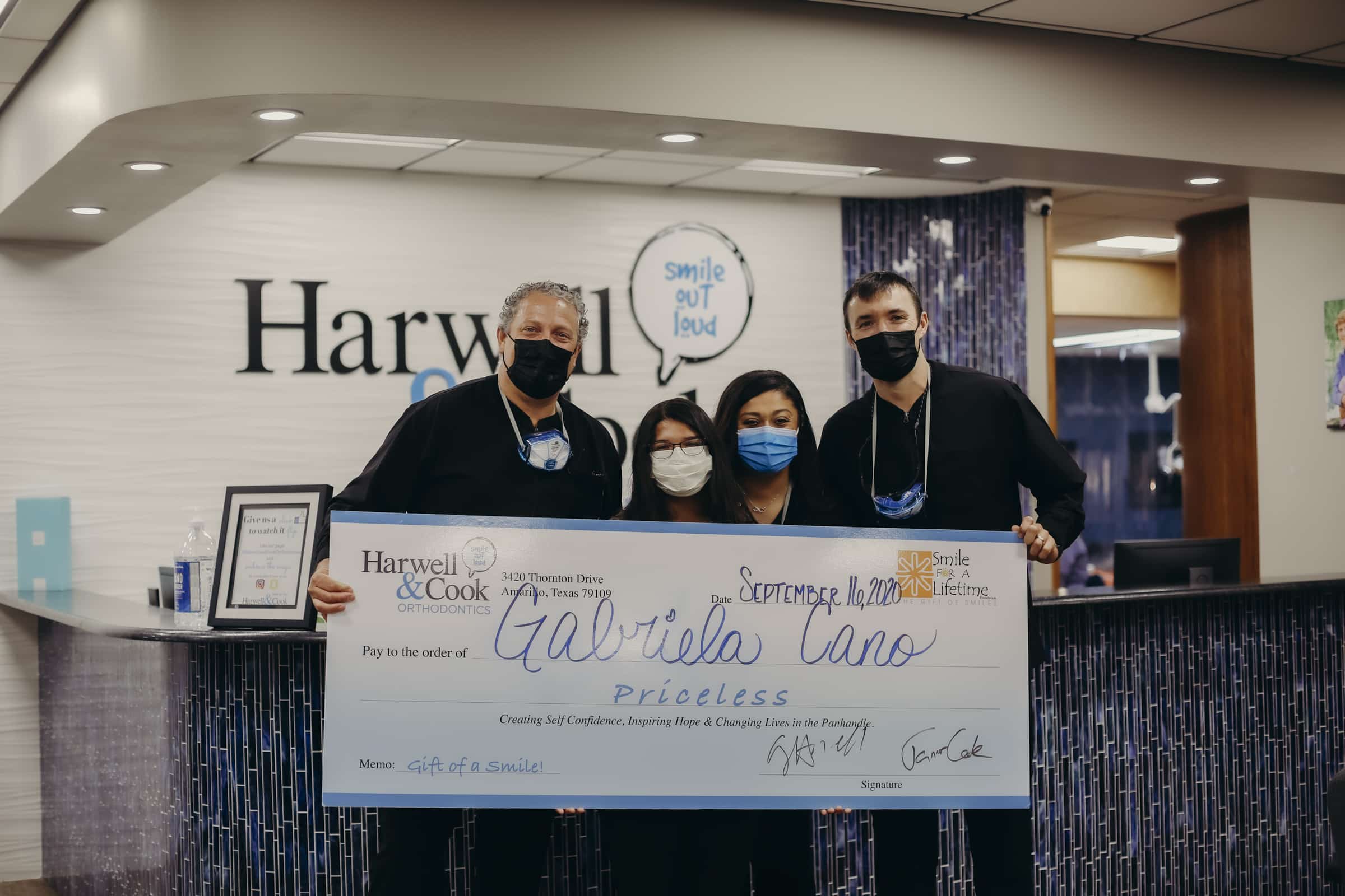 Dr. Harwell and Cook with group of staff members holding a large check. | Harwell & Cook Orthodontics