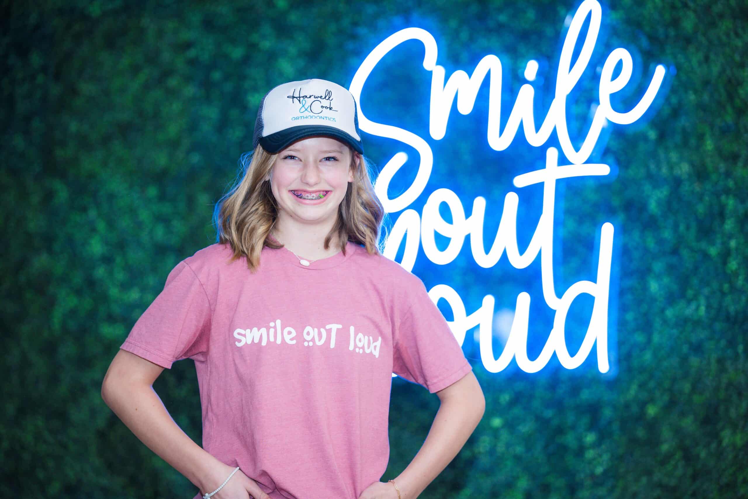 A girl in a pink t-shirt posing in front of a blue background. | Harwell & Cook Orthodontics