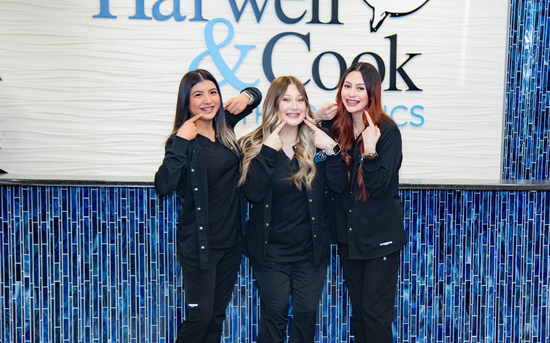 Three women standing together in front of the practice wall. | Harwell & Cook Orthodontics