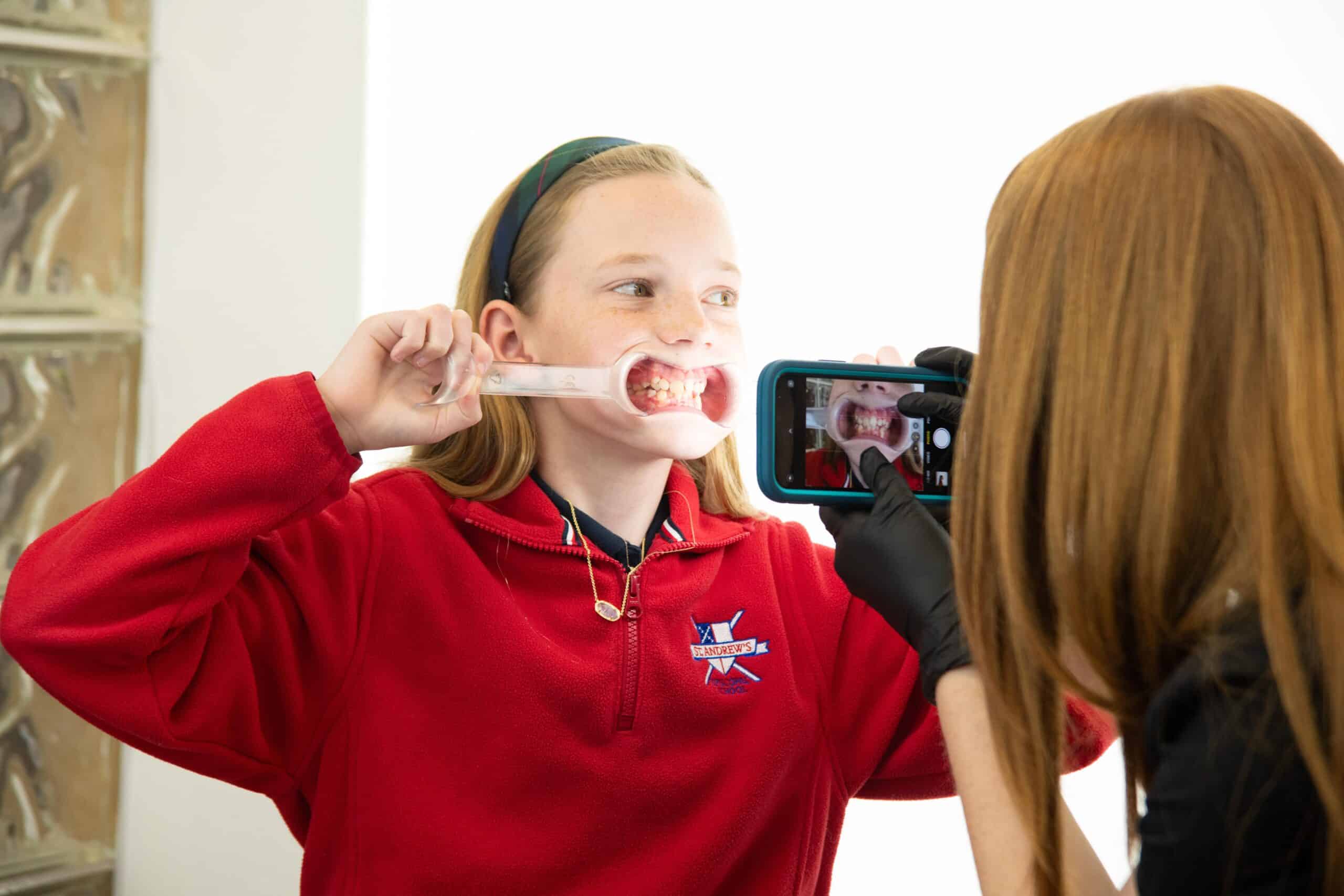 A young girl holding a dental aligner device. | Harwell & Cook Orthodontics